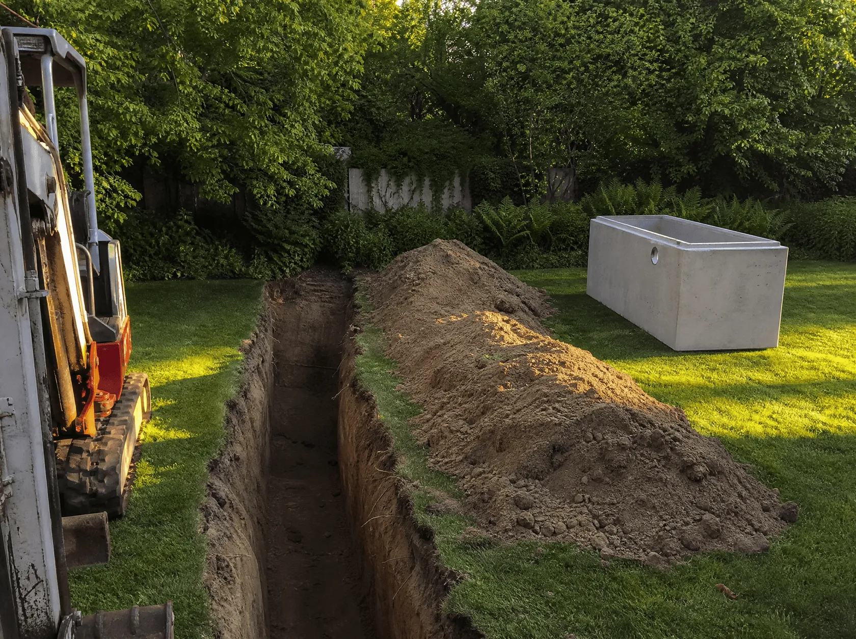 An open trench cut across a lawn beside a new precast concrete tank waiting to be lowered in